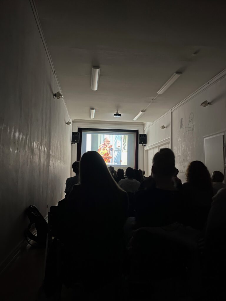 Dunkler Raum mit Publikum, das auf einer Leinwand einen Film schaut